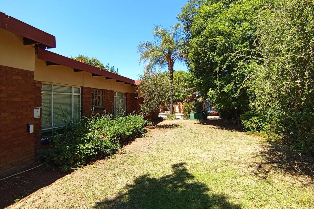 A view of the rear exterior of the house featuring exposed brick walls, large windows, and a spacious garden area.