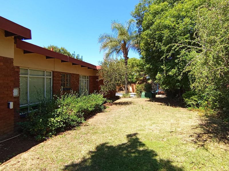 A view of the rear exterior of the house featuring exposed brick walls, large windows, and a spacious garden area.