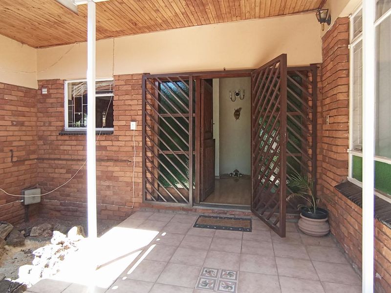 Covered patio area featuring exposed brick walls, timber ceiling, and tiled flooring, providing a sheltered entrance to the home.