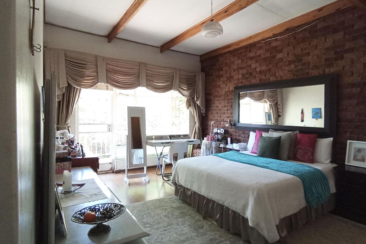 Spacious bedroom featuring an exposed brick feature wall, timber ceiling beams, and direct access to a private balcony through sliding glass doors.