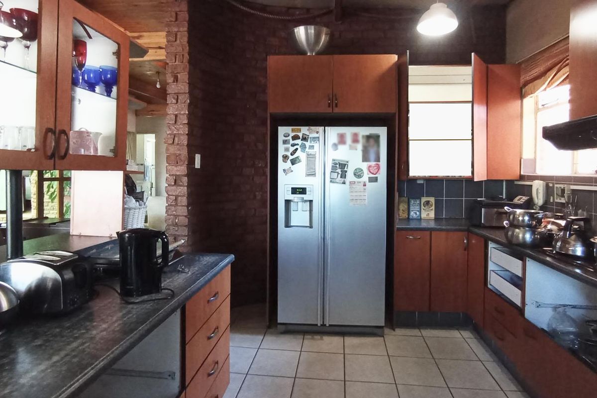 A functional kitchen featuring wooden cabinetry, dark laminate countertops, tiled flooring, and a distinctive exposed brick wall element.