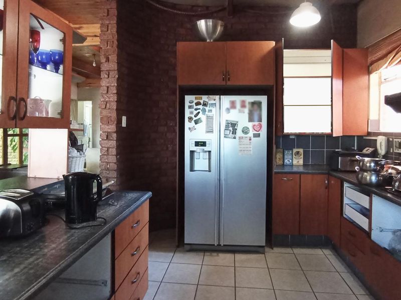 A functional kitchen featuring wooden cabinetry, dark laminate countertops, tiled flooring, and a distinctive exposed brick wall element.