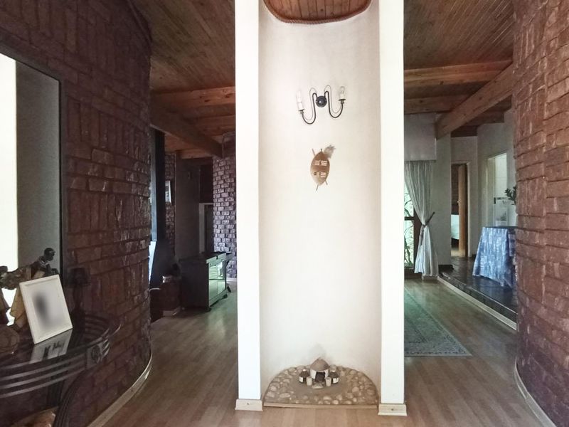 A spacious hallway featuring rustic exposed brick walls, warm timber beam ceilings, and laminate flooring, creating a unique architectural transition between living areas.