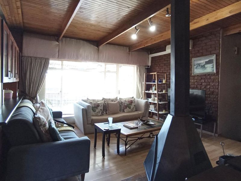 Spacious living room featuring exposed brick walls, timber beam ceilings, and a central freestanding fireplace, creating a warm and rustic atmosphere.