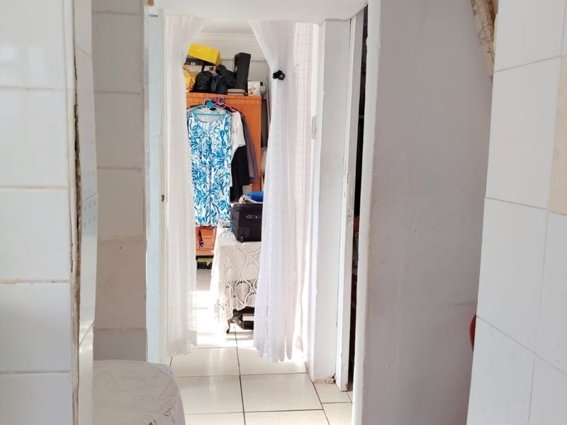 A narrow hallway featuring ceramic floor tiles and tiled wall finishes, providing access to adjacent living spaces.