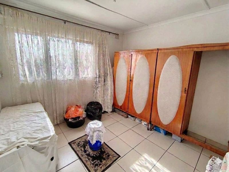 A bedroom featuring tiled flooring, a built-in wardrobe, and large windows, offering a functional space ready for modernization and cosmetic updates.