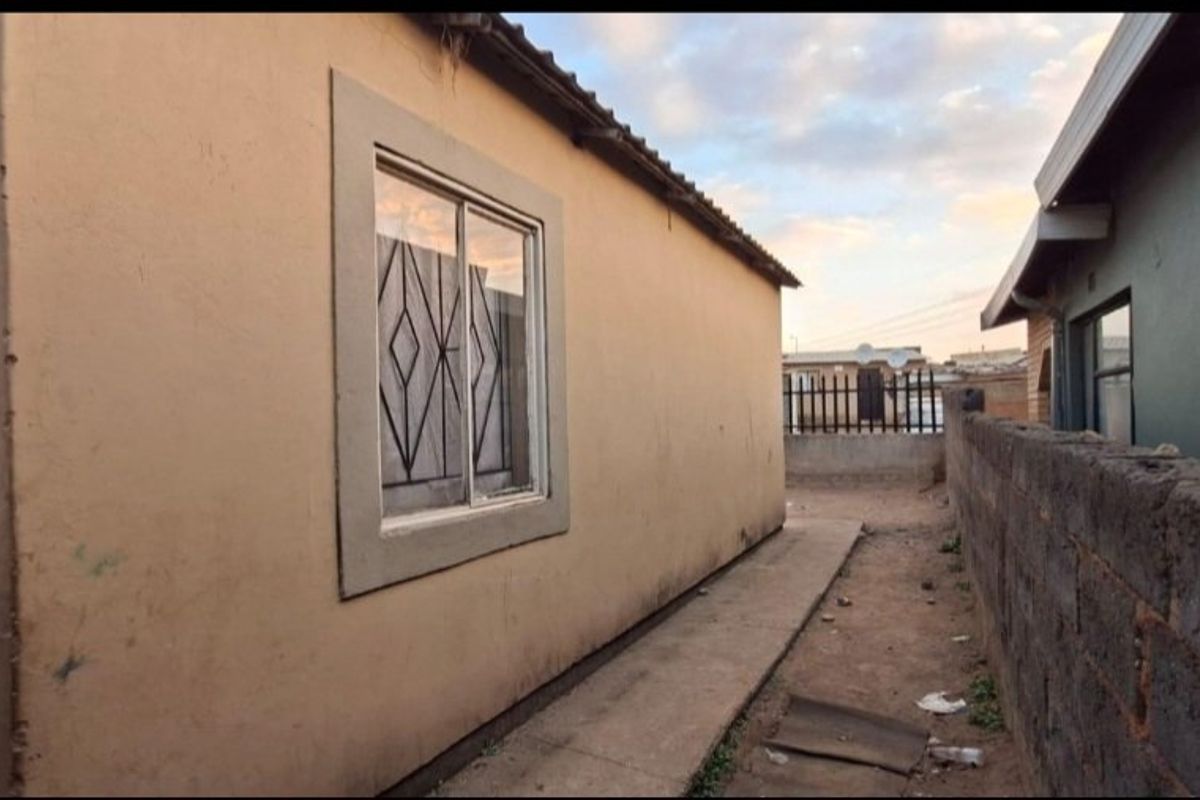 Side view of the property showing a concrete pathway, exterior wall with security-fitted window, and a boundary wall separating the neighboring property.