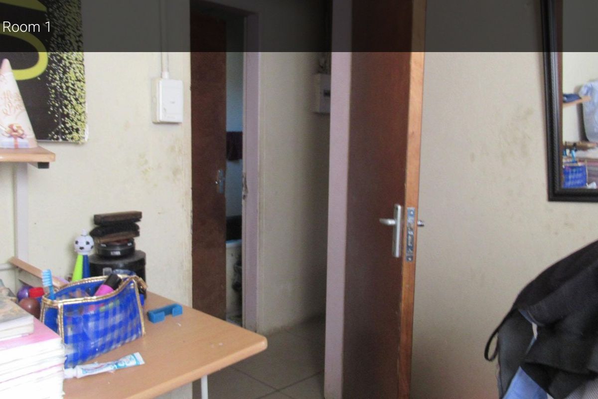 A bedroom interior featuring tiled flooring and wooden doors, showing signs of wall staining and general wear.