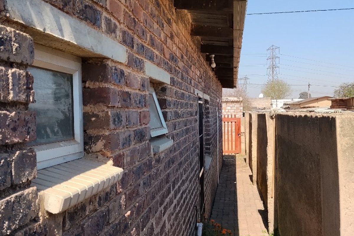 A narrow side passage featuring face brick exterior walls, concrete boundary fencing, and a paved walkway with exposed timber roof rafters.