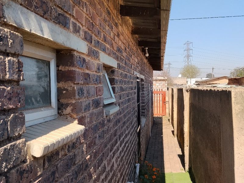 A narrow side passage featuring face brick exterior walls, concrete boundary fencing, and a paved walkway with exposed timber roof rafters.