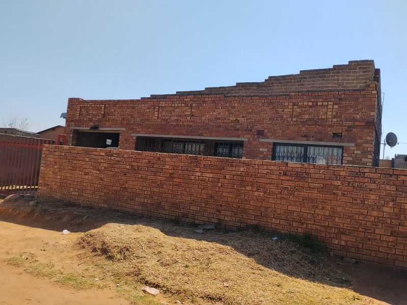 Front exterior view of a face brick house featuring a perimeter wall, security bars on windows, and an unfinished roof parapet.
