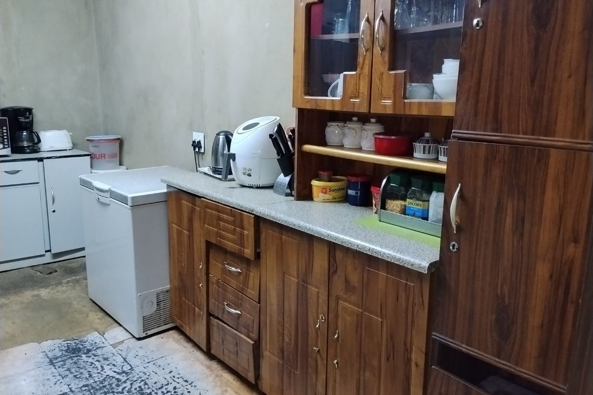 A functional kitchen area featuring traditional wooden cabinetry, ample storage space, and a laminate countertop, requiring cosmetic updates to modernize the finishes.