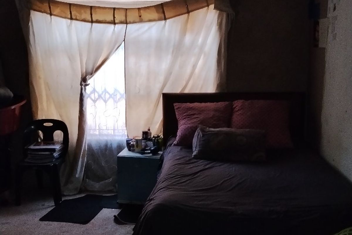 A dimly lit bedroom featuring exposed timber ceiling beams and security bars on the window, requiring significant cosmetic updates and improved lighting.