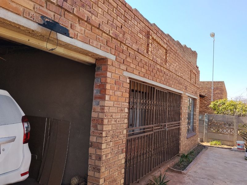 Front exterior view of a face brick house featuring a security gate, concrete driveway, and perimeter walling.