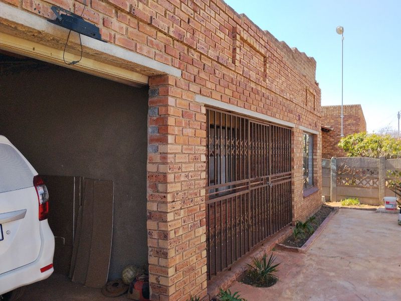 Front exterior view of a face brick house featuring a security gate, concrete driveway, and unfinished plasterwork on the garage wall.