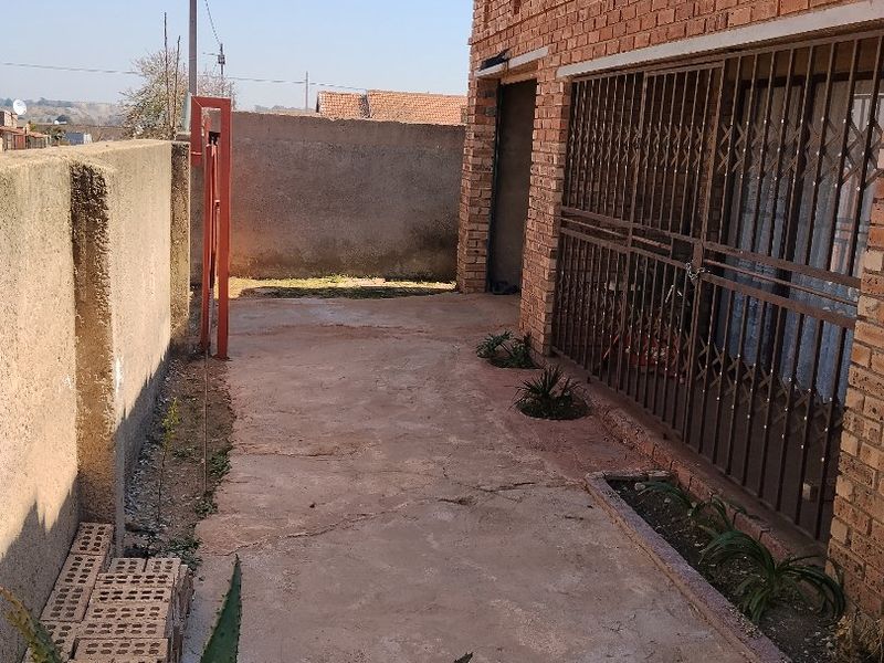 A rear exterior view showing a face brick wall, security gate, and concrete paved area with a boundary wall.