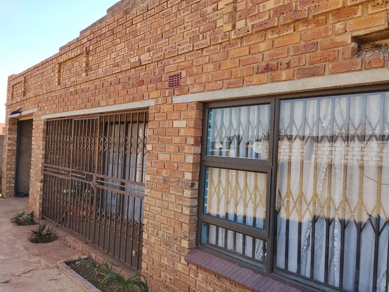 Exterior view of a face brick house featuring metal security gates and aluminium window frames.