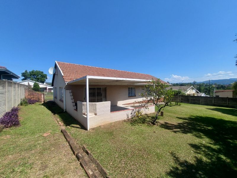 Rear view of the house featuring a covered patio area, tiled roof, and a spacious garden with perimeter boundary walls.