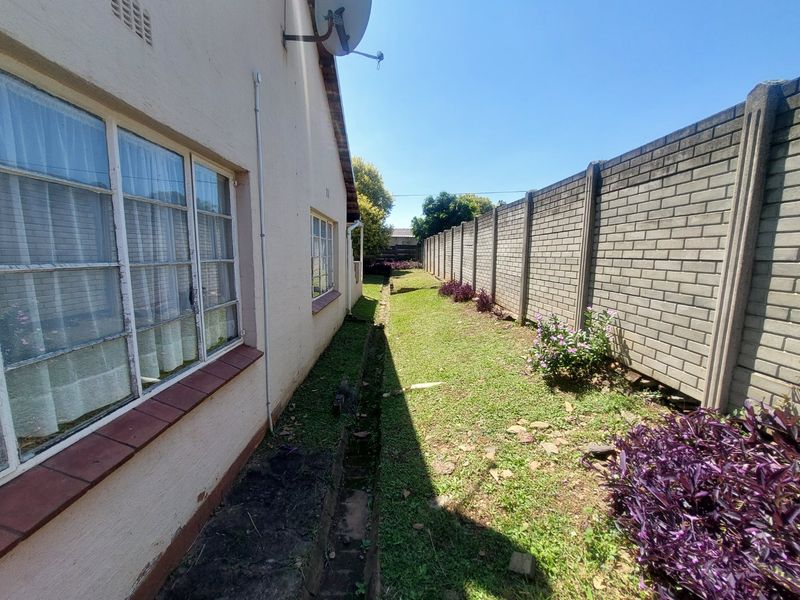 A narrow side garden area featuring a long brick boundary wall and exterior access to the side of the house with steel-framed windows.