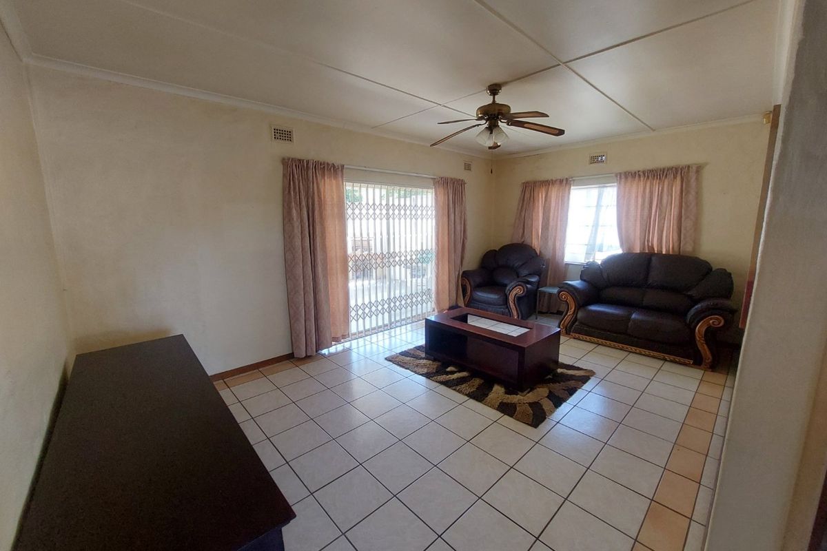 A living room featuring tiled flooring, a ceiling fan, and a sliding glass door with a security gate leading to the exterior.