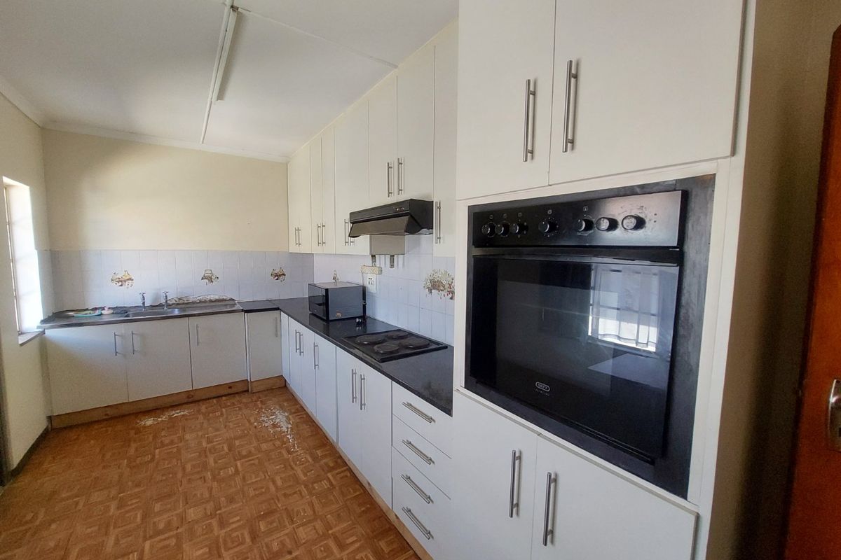 A functional kitchen featuring built-in cabinetry, a wall-mounted oven, electric hob, and a stainless steel sink with a tiled backsplash.