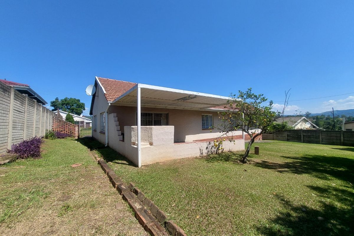 Rear view of the house featuring a covered patio, tiled roof, and a spacious garden enclosed by precast concrete boundary walls.