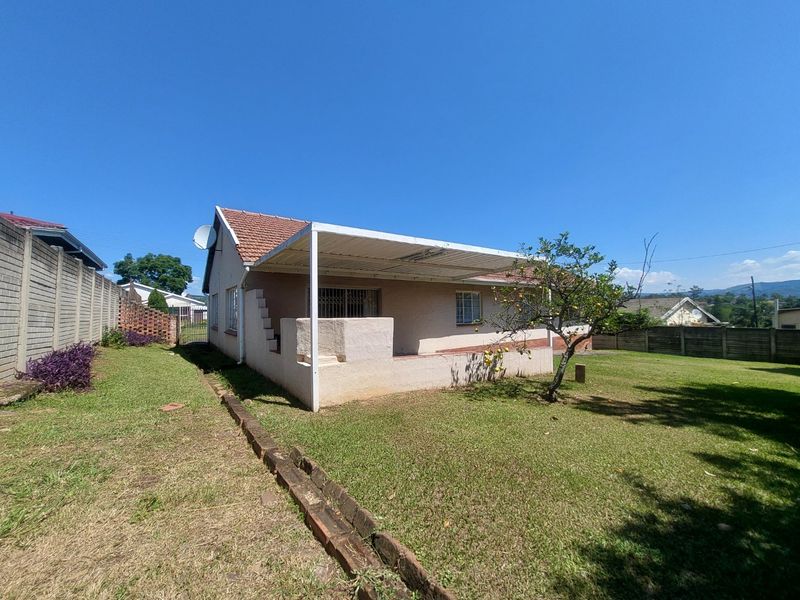 Rear view of the house featuring a covered patio, tiled roof, and a spacious garden enclosed by precast concrete boundary walls.