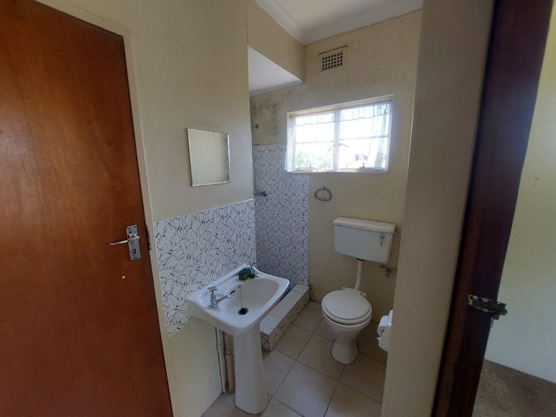 A functional bathroom featuring a pedestal basin, toilet, and shower cubicle, requiring cosmetic updates to improve the overall condition and aesthetic appeal.