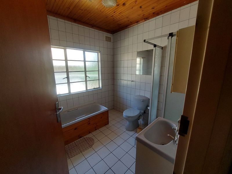 A functional bathroom featuring a bathtub, shower enclosure, toilet, and vanity basin, finished with tiled surfaces and a timber ceiling.