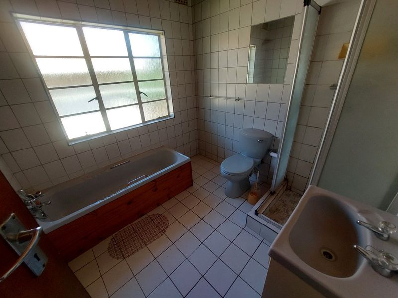 A functional bathroom featuring a bathtub, shower enclosure, toilet, and washbasin with dated wall and floor tiling.
