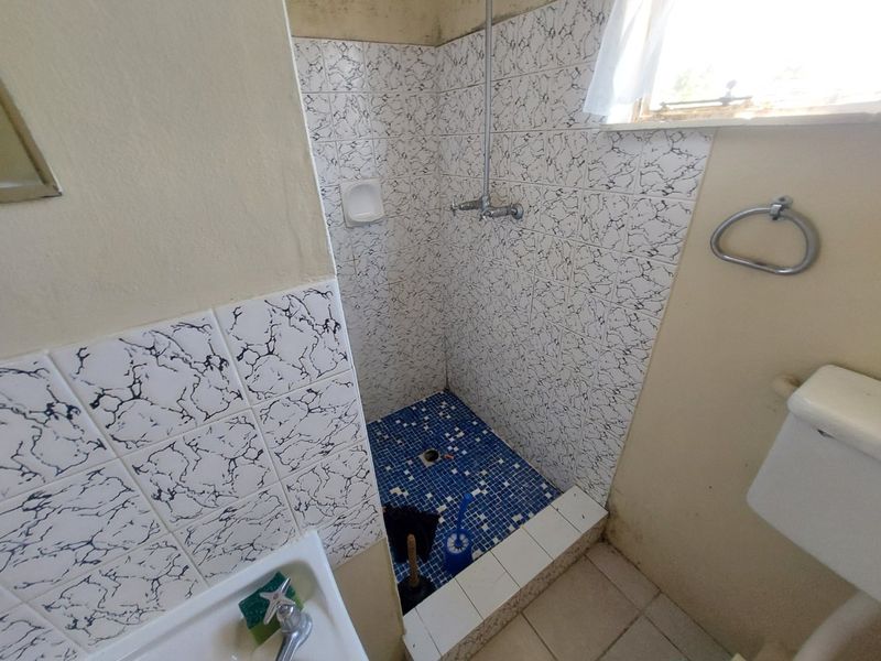 A dated bathroom featuring a tiled shower enclosure with mosaic flooring, a standard toilet, and wall-mounted fixtures, requiring cosmetic updates to modernize the space.