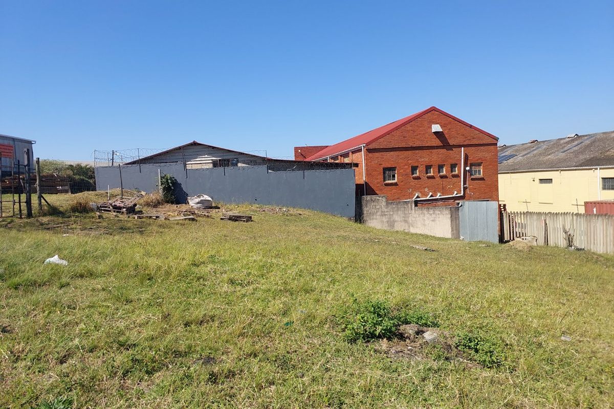Rear view of an industrial property featuring a brick warehouse building, perimeter wall with security fencing, and an expansive unlandscaped grass yard.