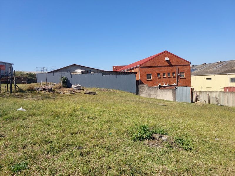 Rear view of an industrial property featuring a brick warehouse building, perimeter wall with security fencing, and an expansive unlandscaped grass yard.