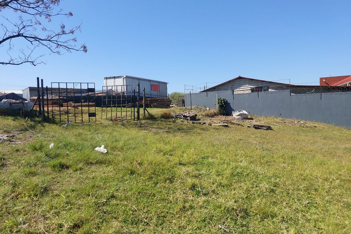 An industrial outdoor yard area featuring a perimeter wall with razor wire, metal gate access, and an industrial storage container on site.