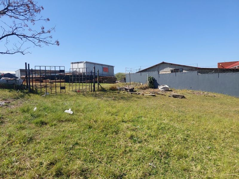 An industrial outdoor yard area featuring a perimeter wall with razor wire, metal gate access, and an industrial storage container on site.