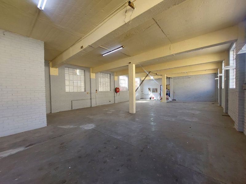 Spacious industrial utility area featuring exposed concrete ceilings, painted brick walls, and durable concrete flooring, suitable for warehouse or workshop use.