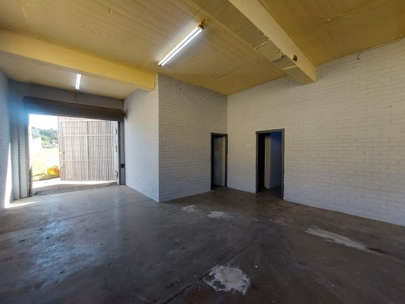 Spacious industrial utility area featuring painted brick walls, concrete flooring, and a large roller shutter door for easy access.
