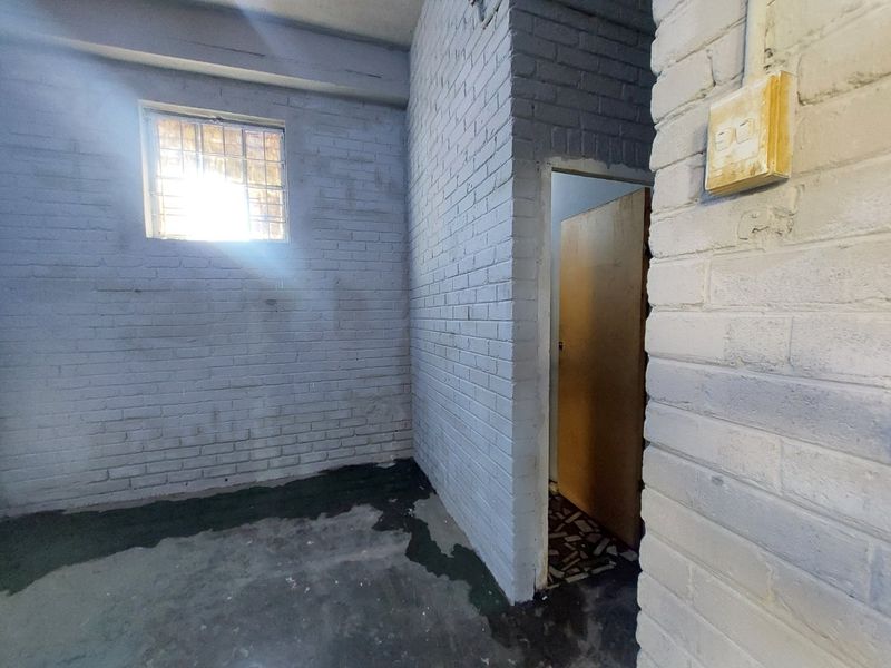 An industrial utility space featuring painted brick walls, a window with security bars, and exposed electrical infrastructure.