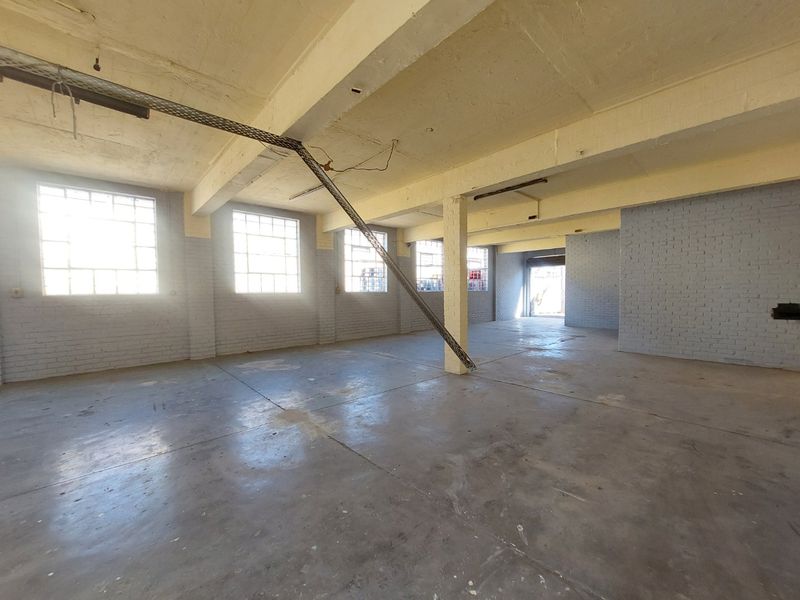 Spacious open-plan industrial unit featuring exposed concrete ceilings, polished concrete flooring, and large steel-framed windows providing ample natural light.