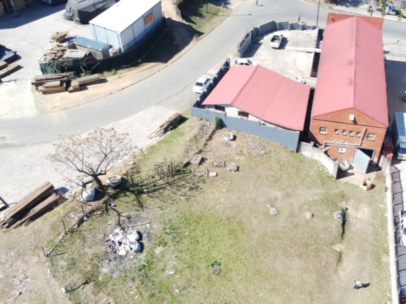 Aerial view of an industrial property featuring multiple brick buildings with metal roofing, paved access areas, and surrounding open land.