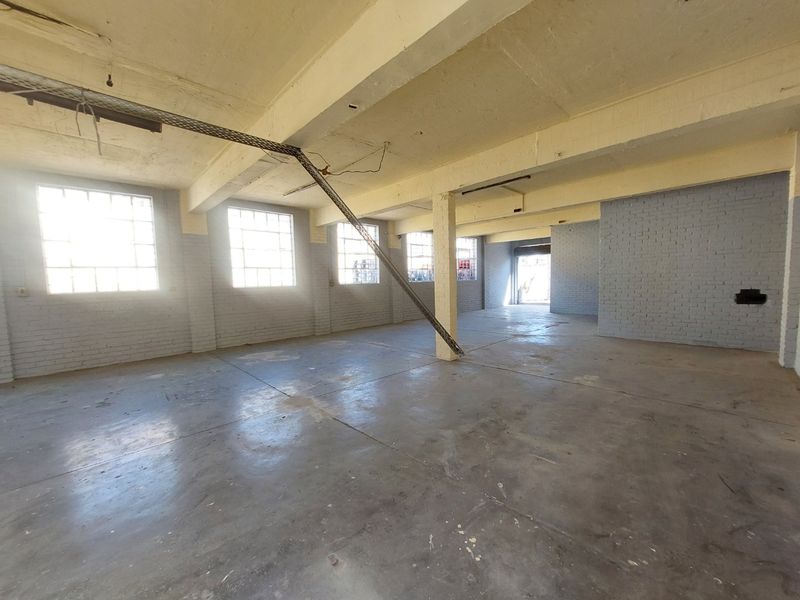 Spacious industrial utility space featuring exposed concrete ceilings, structural columns, and large steel-framed windows, offering a versatile open-plan layout.