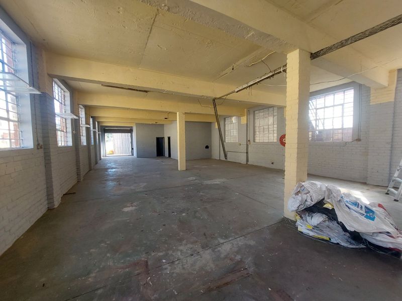 Spacious industrial utility area featuring exposed concrete beams, brick columns, and large steel-framed windows, offering a versatile open-plan layout.
