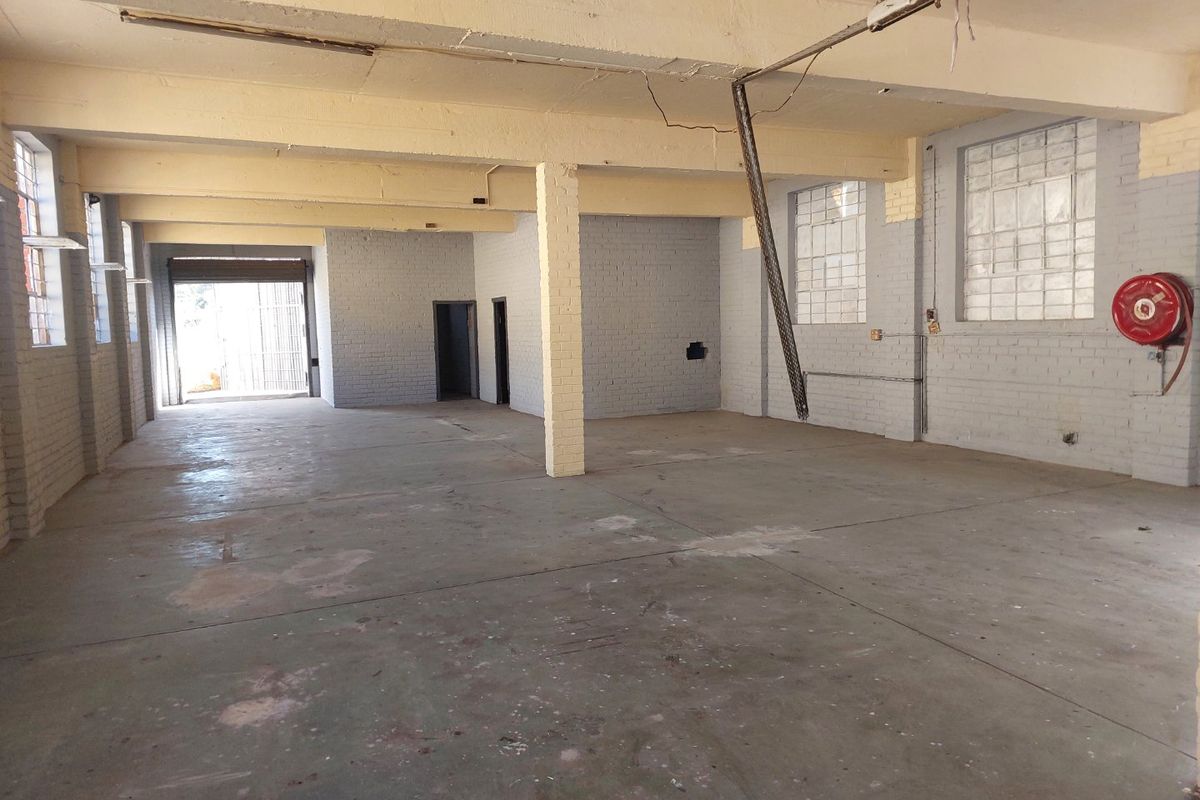 Spacious industrial utility area featuring exposed concrete beams, painted brick walls, and durable concrete flooring, suitable for workshop or storage use.
