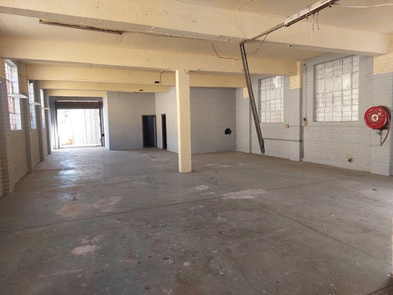 Spacious industrial utility area featuring exposed concrete beams, painted brick walls, and durable concrete flooring, suitable for workshop or storage use.