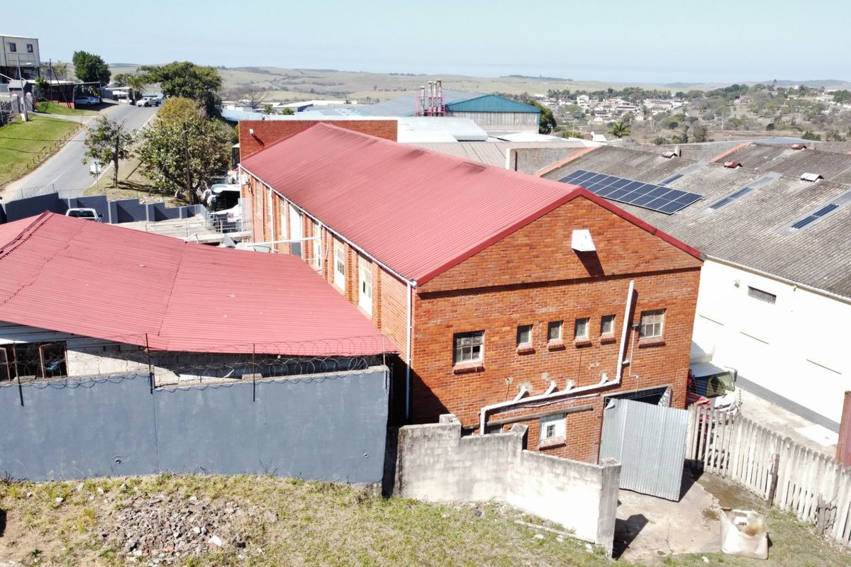Aerial view of an industrial property featuring a brick building with a red corrugated metal roof and integrated solar panels.