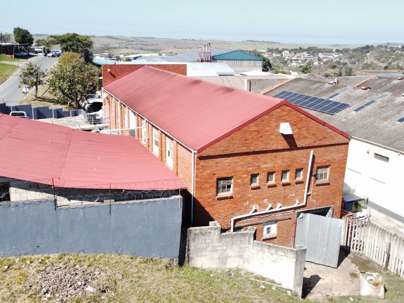 Aerial view of an industrial property featuring a brick building with a red corrugated metal roof and integrated solar panels.