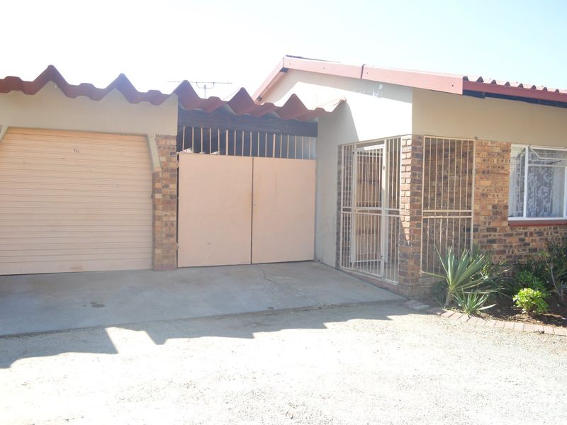 Front elevation of a townhouse featuring a single garage, secure gated entrance, and brick facade with protective security bars on windows.
