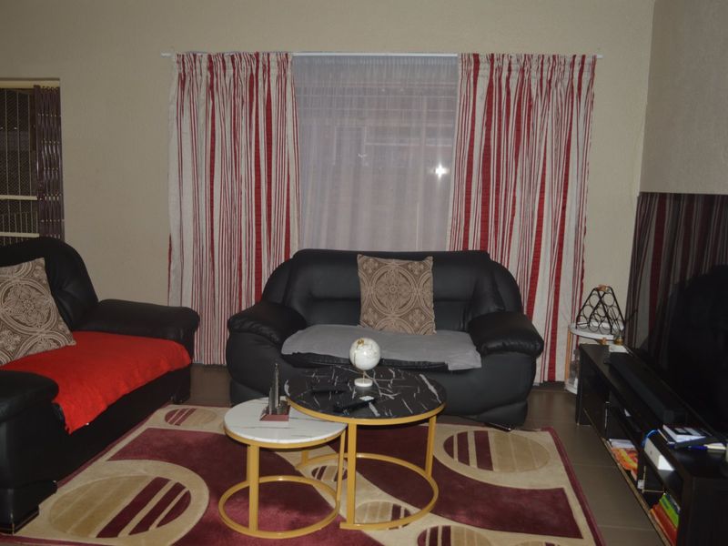 A living room featuring tiled flooring and a window with curtain tracks, providing a functional space for relaxation.