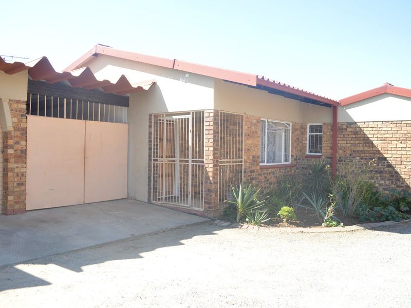 Front elevation of a townhouse featuring brick construction, a secure entrance gate, and an attached garage with a corrugated roof.