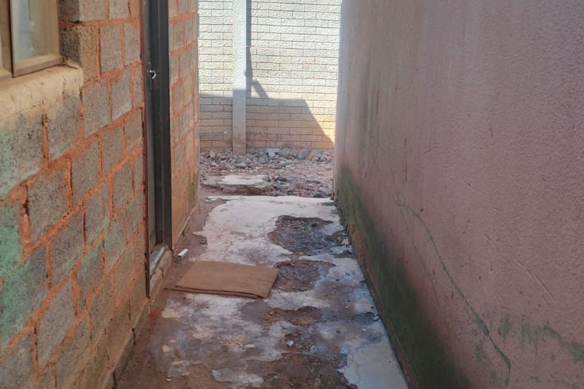 A narrow side passage featuring exposed brickwork and a damaged concrete pathway leading to a rear boundary wall.